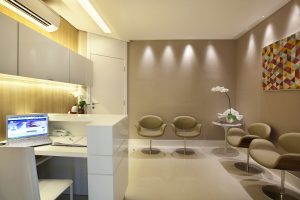 Recepção de consultório dentário com paredes revestidas em papel de parede. Destaque para o efeito das luminárias na parede.
