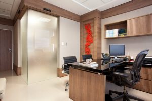 Consultório médico com sala de exames separada por porta de correr de canto em vidro jateado.