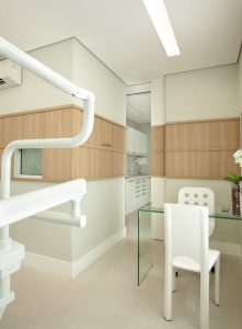 Paredes com faixa em madeira ocultando um armário e emoldurando as janelas de comunicação com a sala de esterilização.