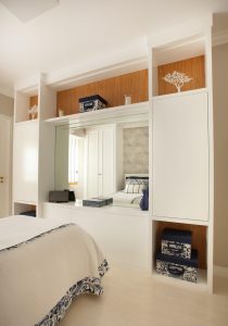 Estante em laca branca com fundo em freijó e espelho em quarto feminino.