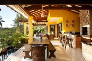 Vista da varanda com destaque para área de churrasqueira e estar ao fundo. Espelho d'água com carpas contorna o ambiente.