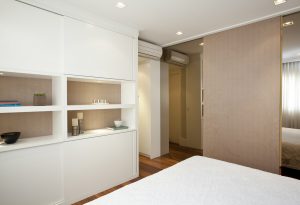 Para dar leveza, os armários na frente da cama possuem nichos revestidos em camurça. Separando o quarto do closet, a porta de correr em camurça corre sobre os espelhos bronze.