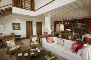 Sala de estar com sala de jantar ao fundo com parede vermelha. Forro de gesso saia e blusa e escada com guarda-corpo em madeira.