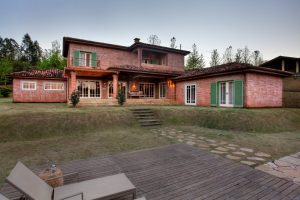 Casa com arquitetura Toscana. Tijolos rústicos e caixilhos de madeira pintados de verde e branco.