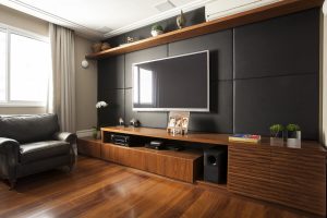 Home theater moderno com painel de couro preto e marcenaria em Nogueira com ripas horizontais.