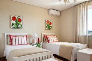 Quarto feminino em tons de branco e bege com detalhes em vermelho. Parede da cabeceira revestida com papel de parede bege.