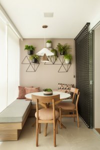 Charmoso cantinho com banco e mesa na varanda com parede rosê e mosaico de plantas